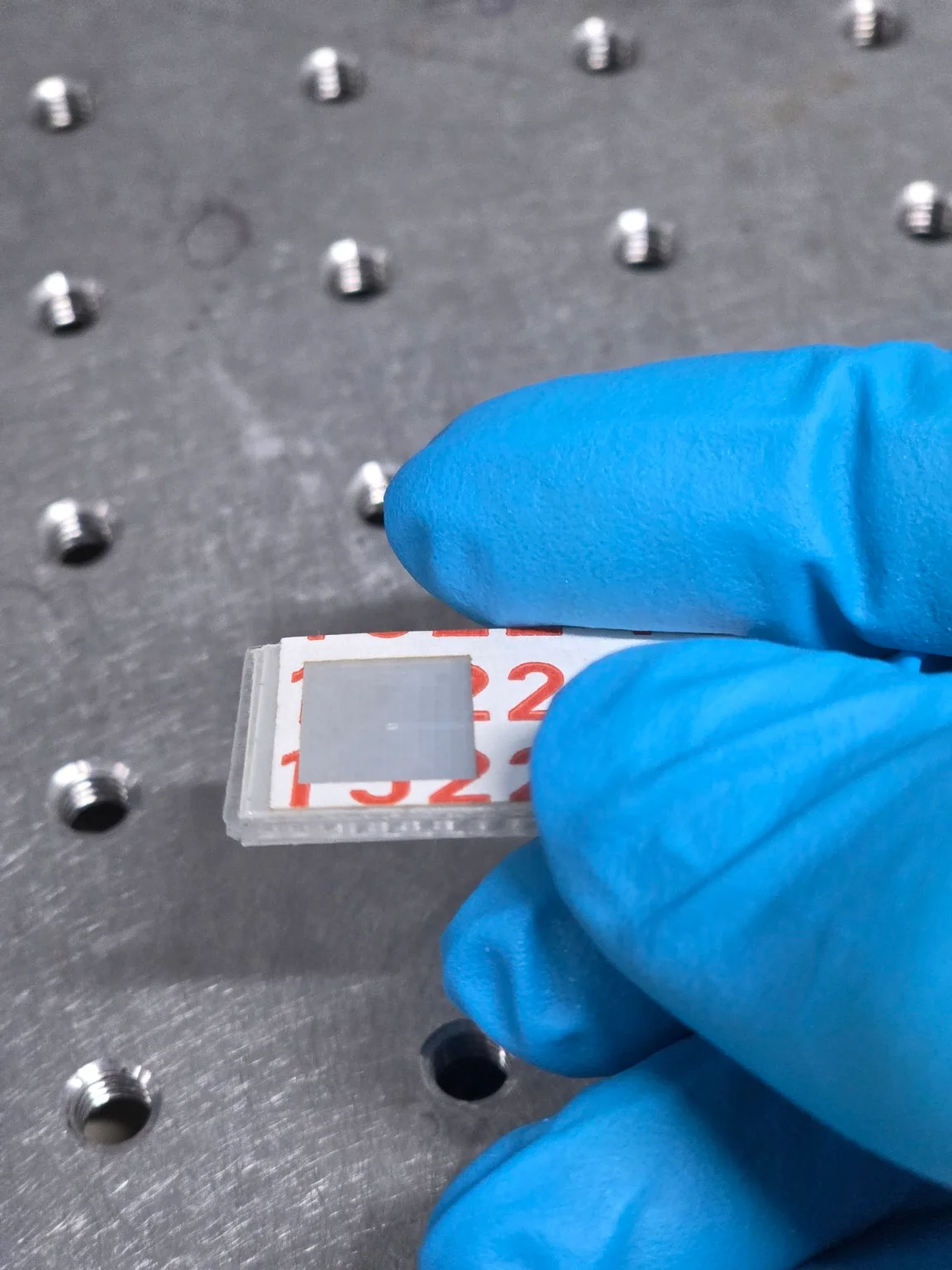 Blue-gloved hand holding a microfluidic prototype above a laboratory work surface
